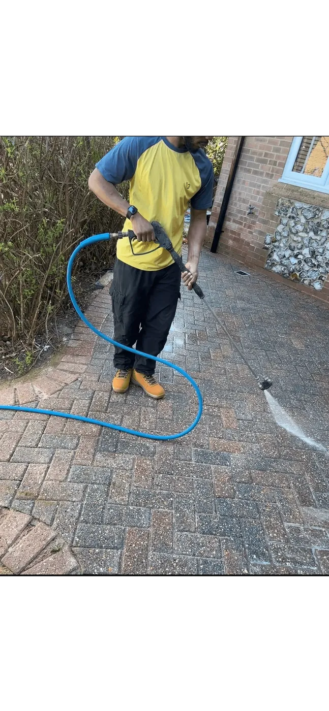 A pressure washer lance clearing a block-paved driveway, with a bright cleaned stripe cut through the dirty paving